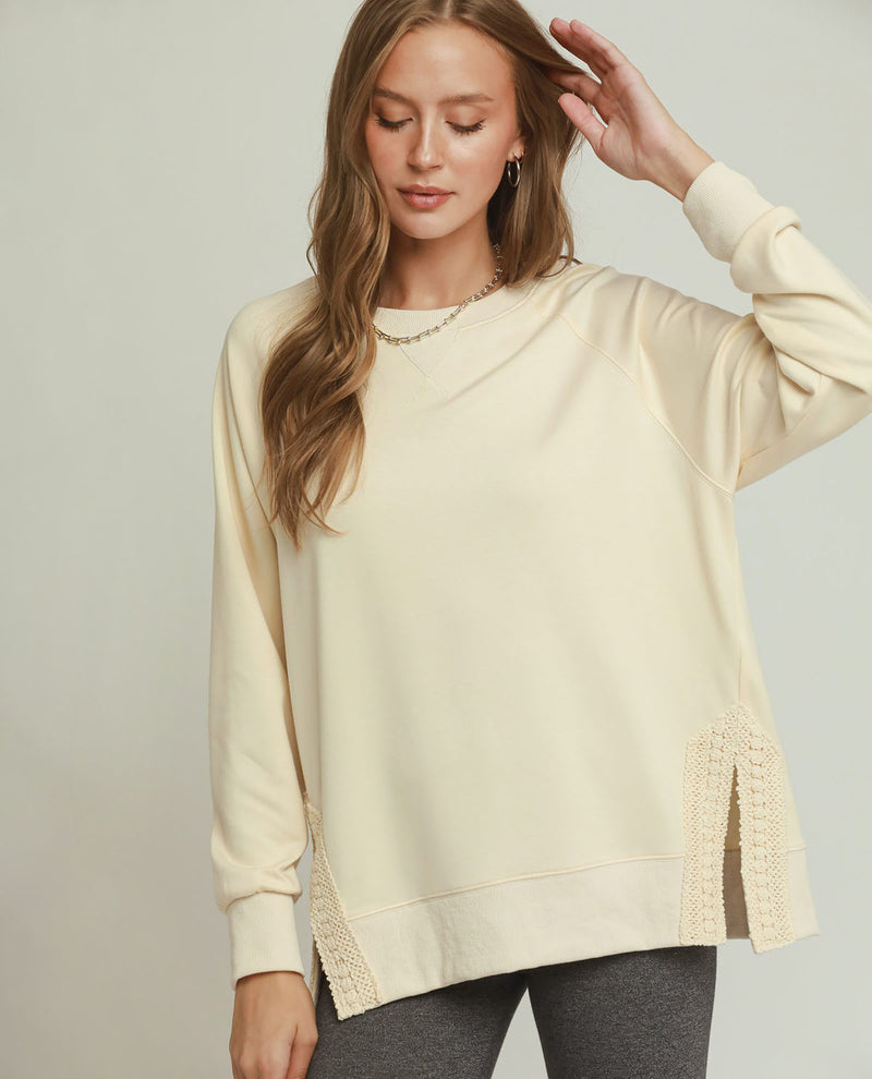 Woman wearing a light-colored sweater with lace details on a plain background
