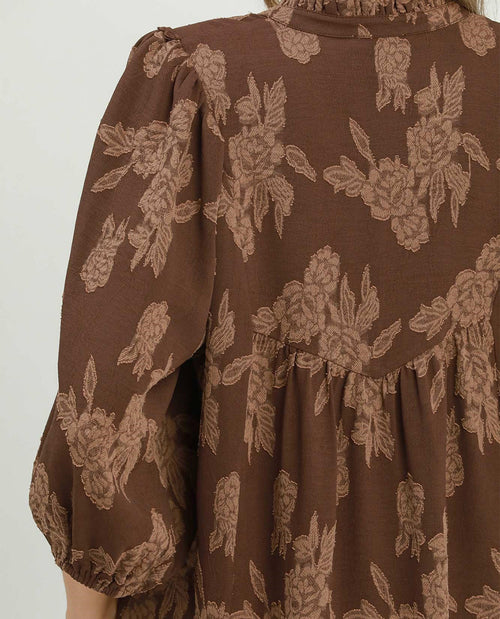 A close-up of a brown dress with a beige floral pattern, featuring puffed sleeves and a gathered waist.