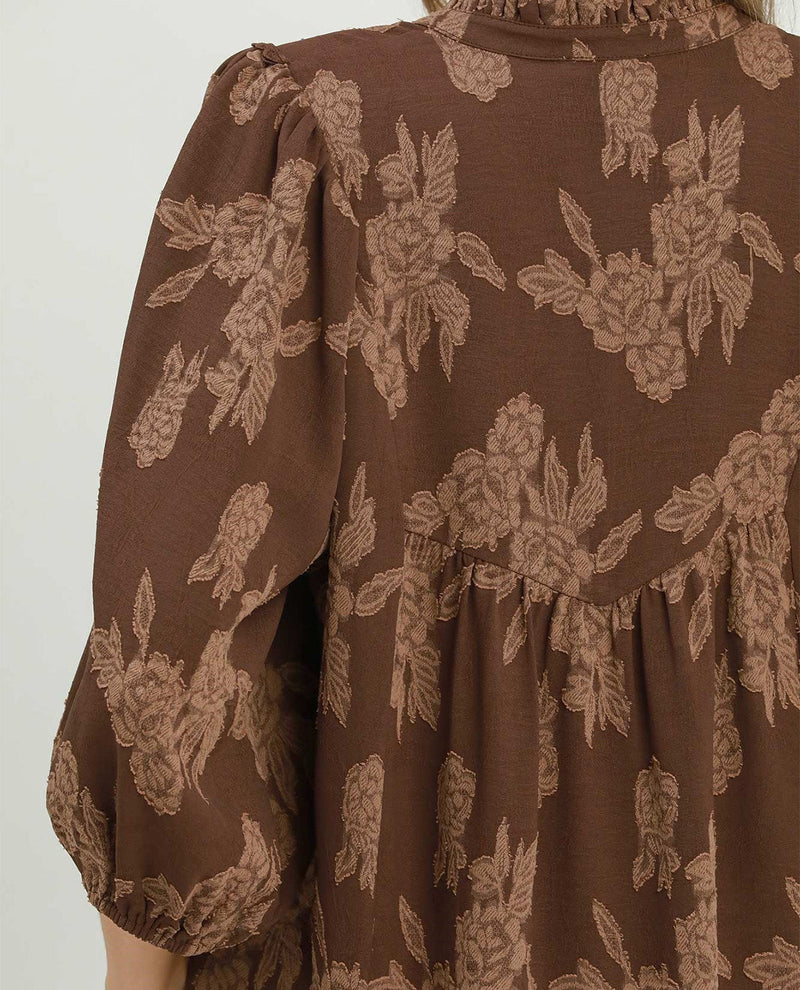 A close-up of a brown dress with a beige floral pattern, featuring puffed sleeves and a gathered waist.