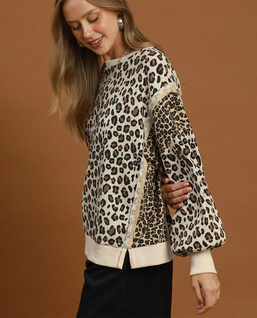 A woman wearing a leopard print long-sleeve top with beige ribbed trim, posed against a solid brown studio background.