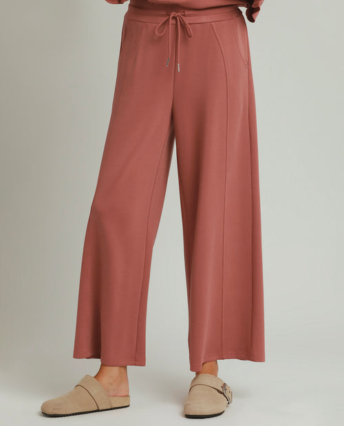 A person wearing dusty rose wide-leg drawstring pants and beige slip-on mule shoes, shown from the waist down against a light gray studio background.