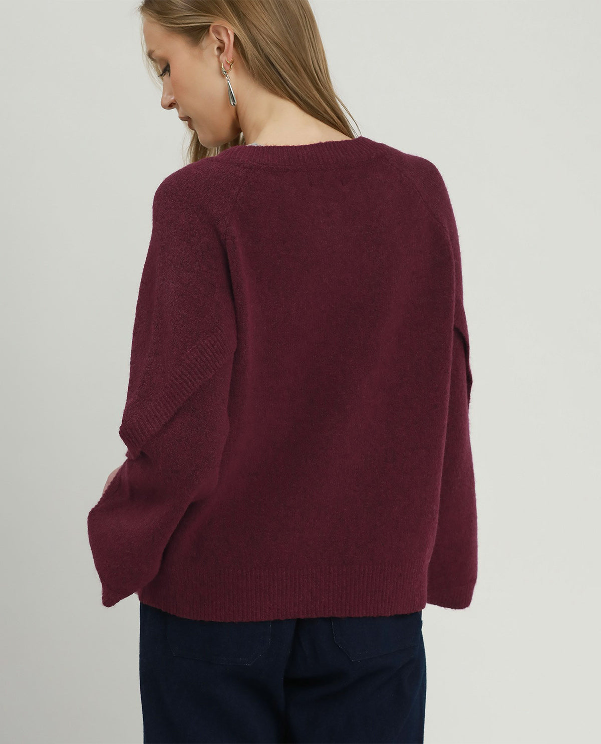 A woman wearing a loose, oversized knit sweater in deep burgundy, shown from the back against a plain light gray studio background.