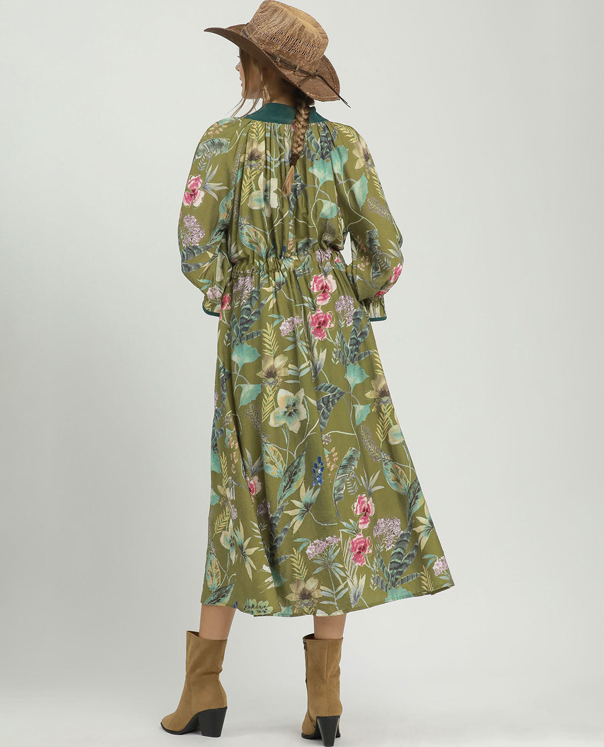 A woman shown from the back wearing a long-sleeve olive green midi dress with a pink and blue floral print, styled with a brown straw hat and tan ankle boots against a light gray studio background.