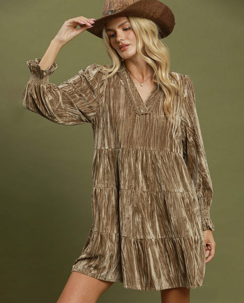 A woman wearing a brown and beige textured tiered dress with long sleeves and a matching brown hat, posing against a solid olive green background.