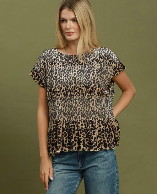 A woman modeling a short-sleeve leopard print top with a ruffled hem, paired with blue jeans, against a solid olive green background.