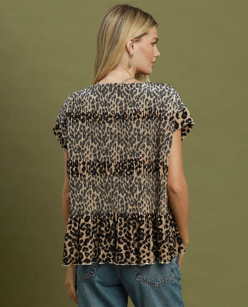 A woman shown from the back wearing a leopard-print short-sleeve blouse with a ruffled hem, paired with blue jeans, against a solid olive green background.