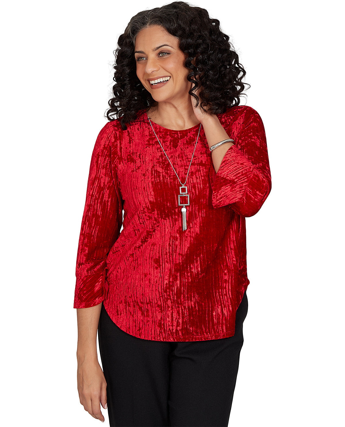 A woman wearing a red crinkle-textured, three-quarter sleeve top and black pants, accessorized with a silver pendant necklace, against a plain white background.