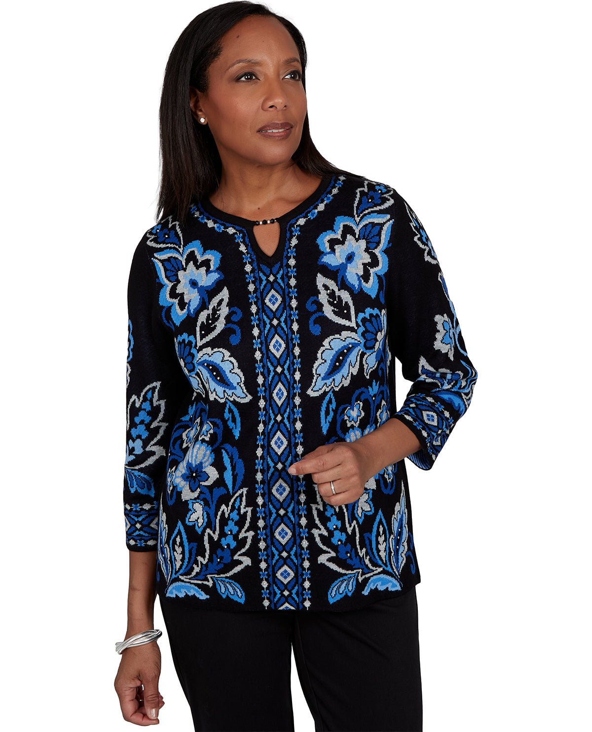 A woman modeling a black long-sleeve top with vibrant blue and white floral and geometric patterns, paired with black pants against a plain white background.