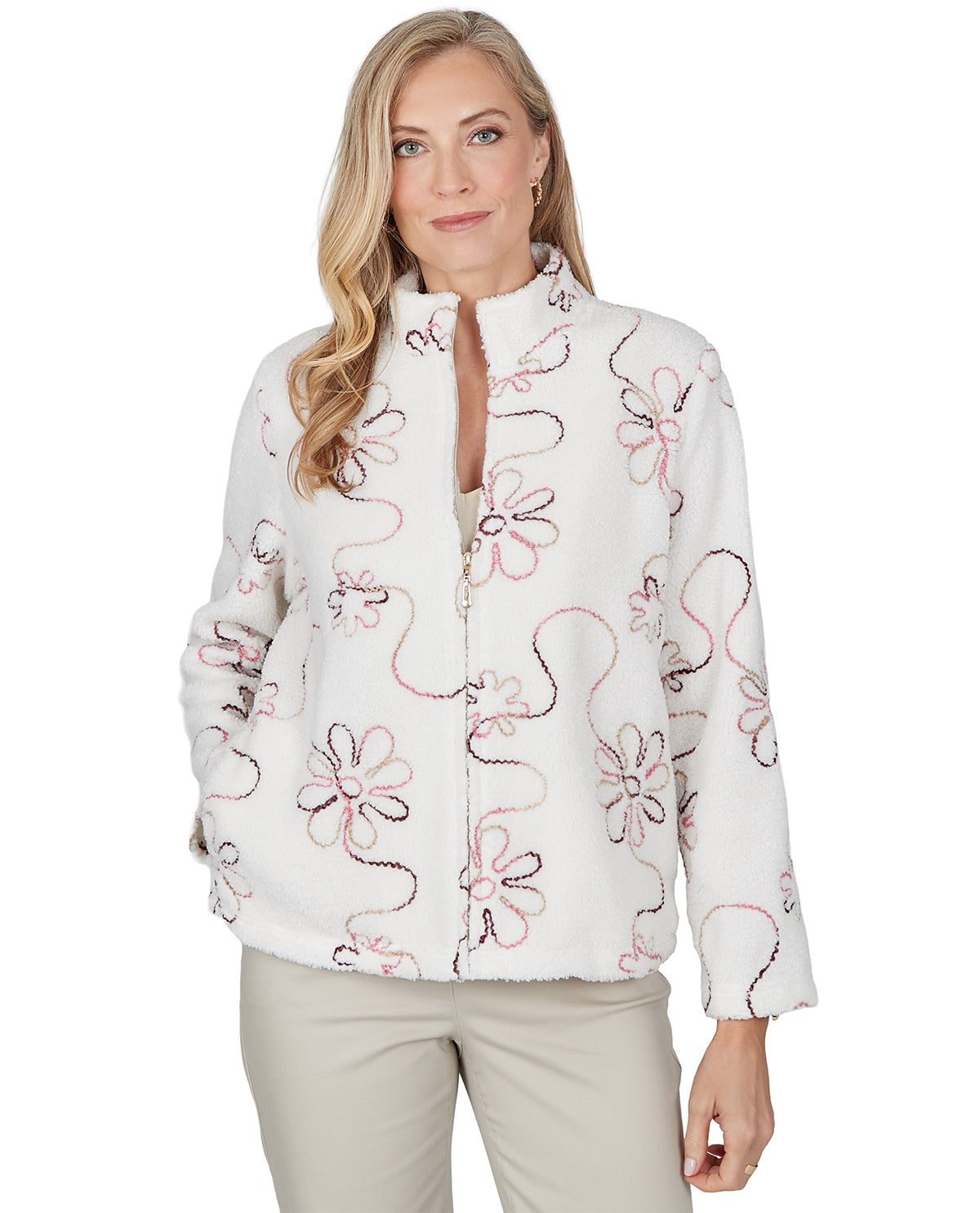 A woman modeling a white zip-up jacket with a pink and black floral pattern, paired with beige pants, against a plain white background.