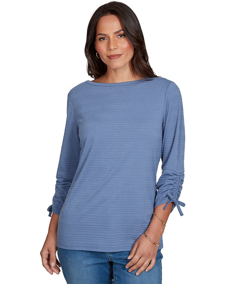 Woman wearing a blue long-sleeve top with tied cuffs on a white background