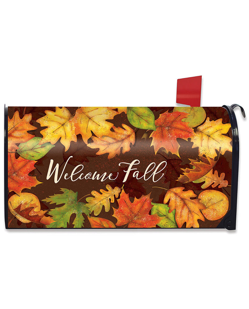 A decorative mailbox cover featuring a fall leaf pattern in orange, yellow, green, and red on a dark brown background, with the words 'Welcome Fall' in white script. A red flag is visible on the right side against a plain white background.