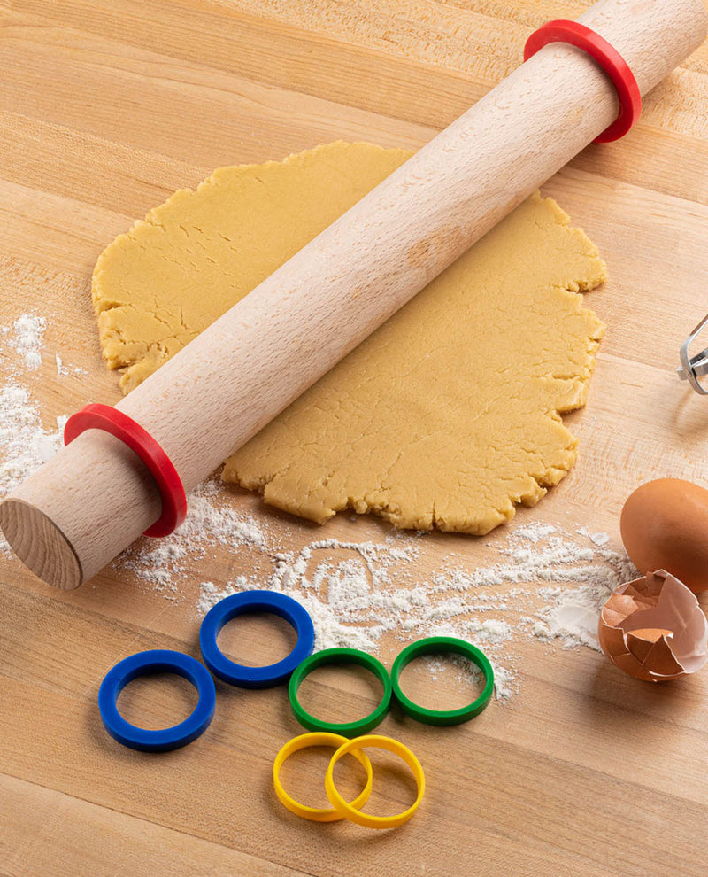 Rolling pin with colorful cookie cutters on a wooden surface with cookie dough.