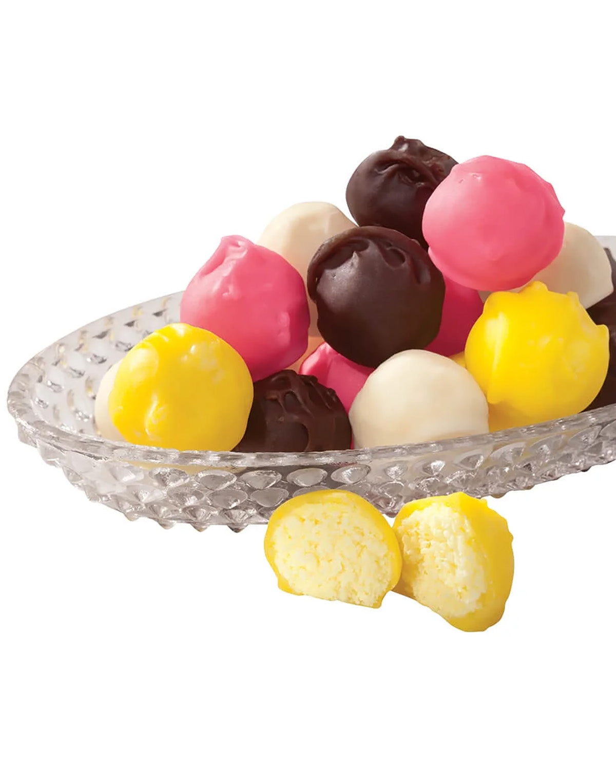 A pile of colorful round chocolate-covered candies in pink, yellow, white, and dark brown, served on a clear textured glass plate with two cut candies showing a soft cream filling in front, on a white background.
