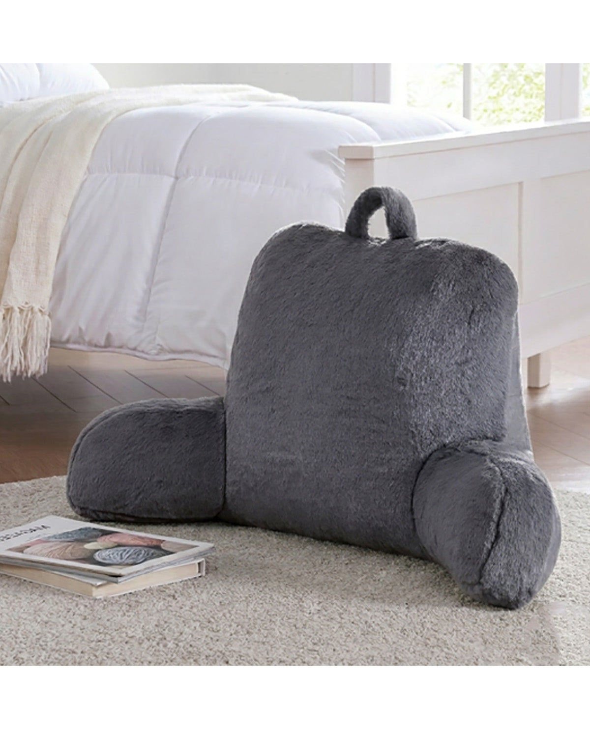Gray backrest pillow on a carpeted floor with a bed and window in the background