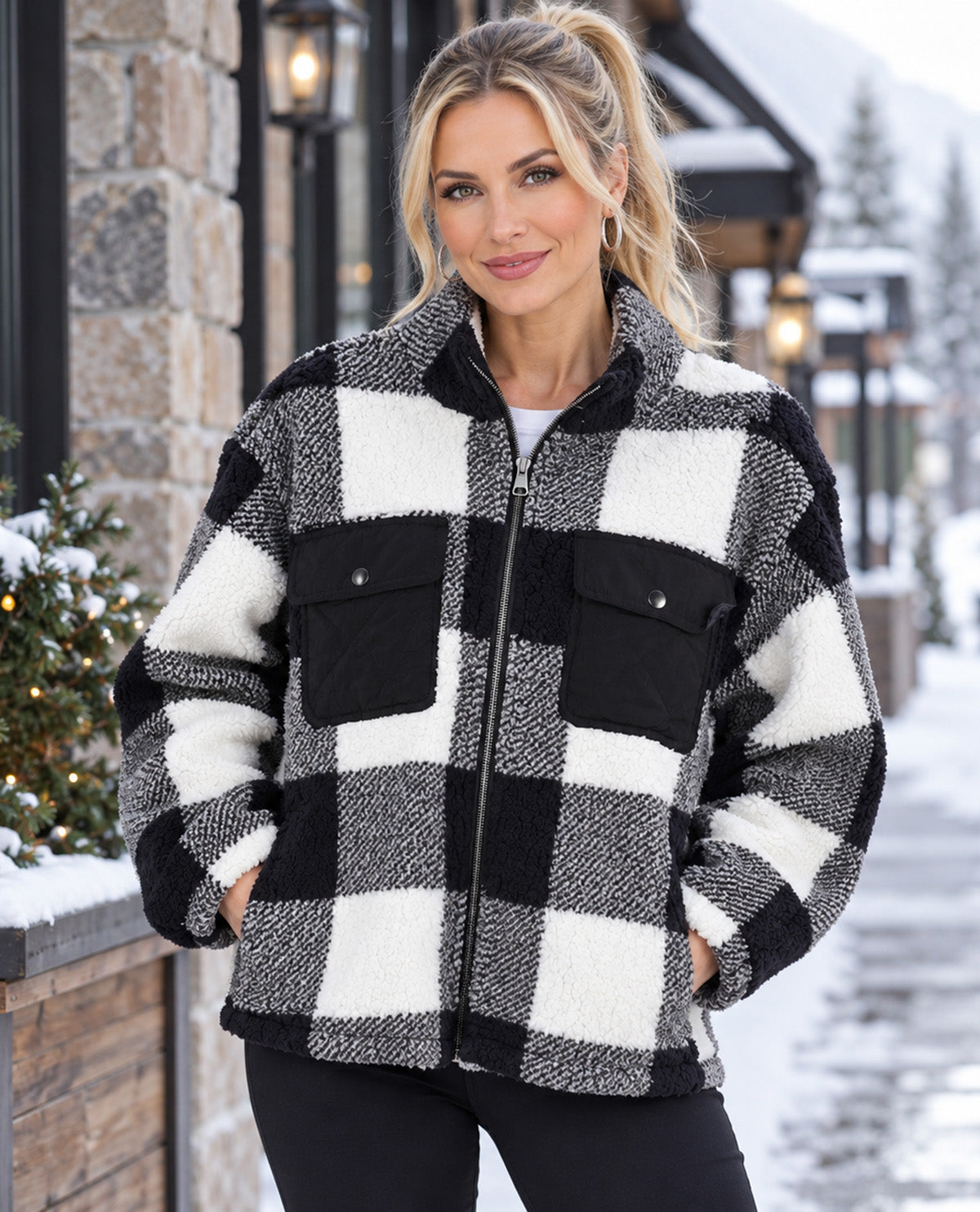 A woman wearing a black and white buffalo plaid sherpa fleece jacket, standing outdoors in a snowy setting.
