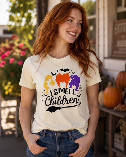 Woman wearing a t-shirt with 'I Smell Children' graphic in an outdoor setting with pumpkins and flowers.