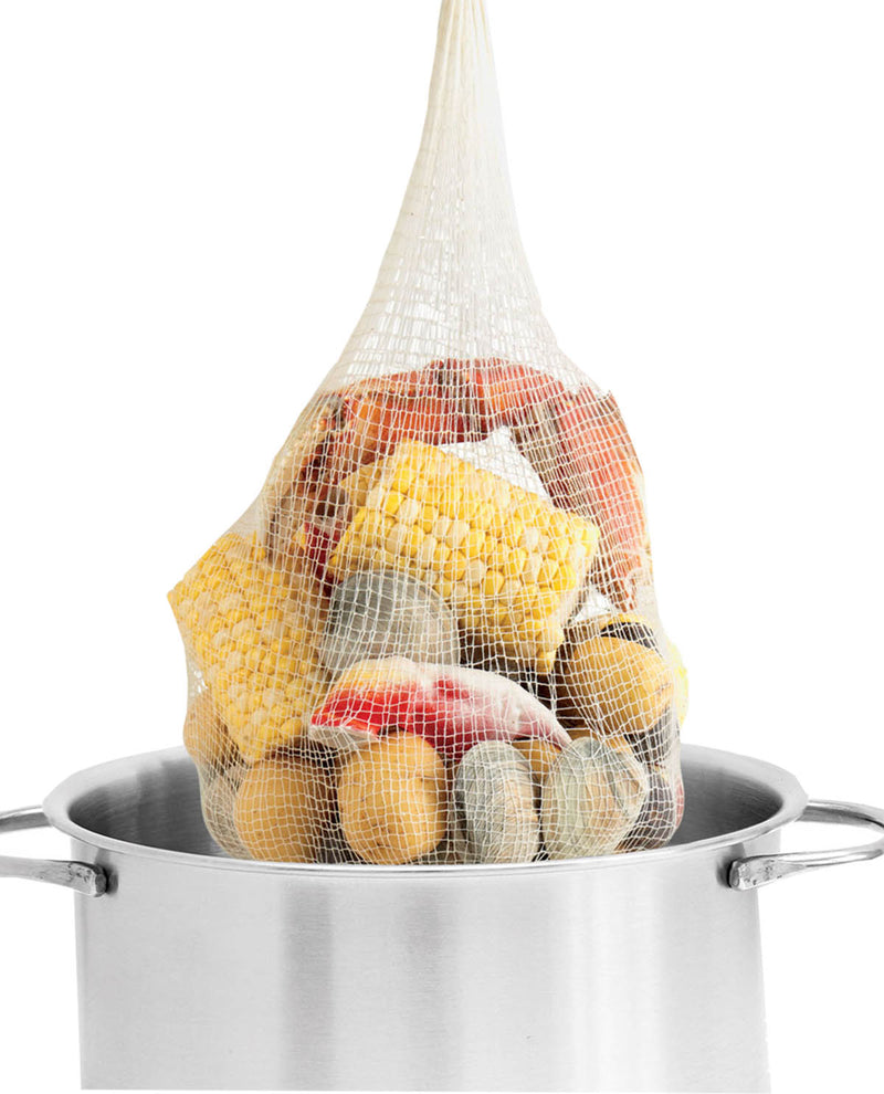 Net bag filled with fruits and vegetables over a pot on a white background