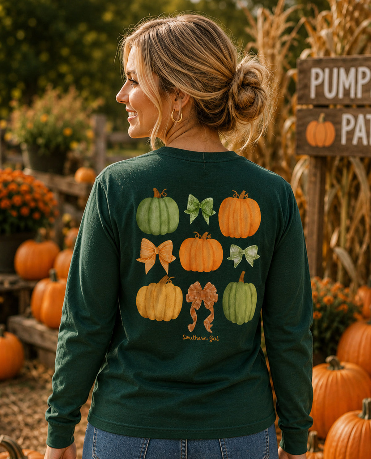 Woman wearing a green long-sleeve shirt with pumpkin and leaf designs in an autumn setting.