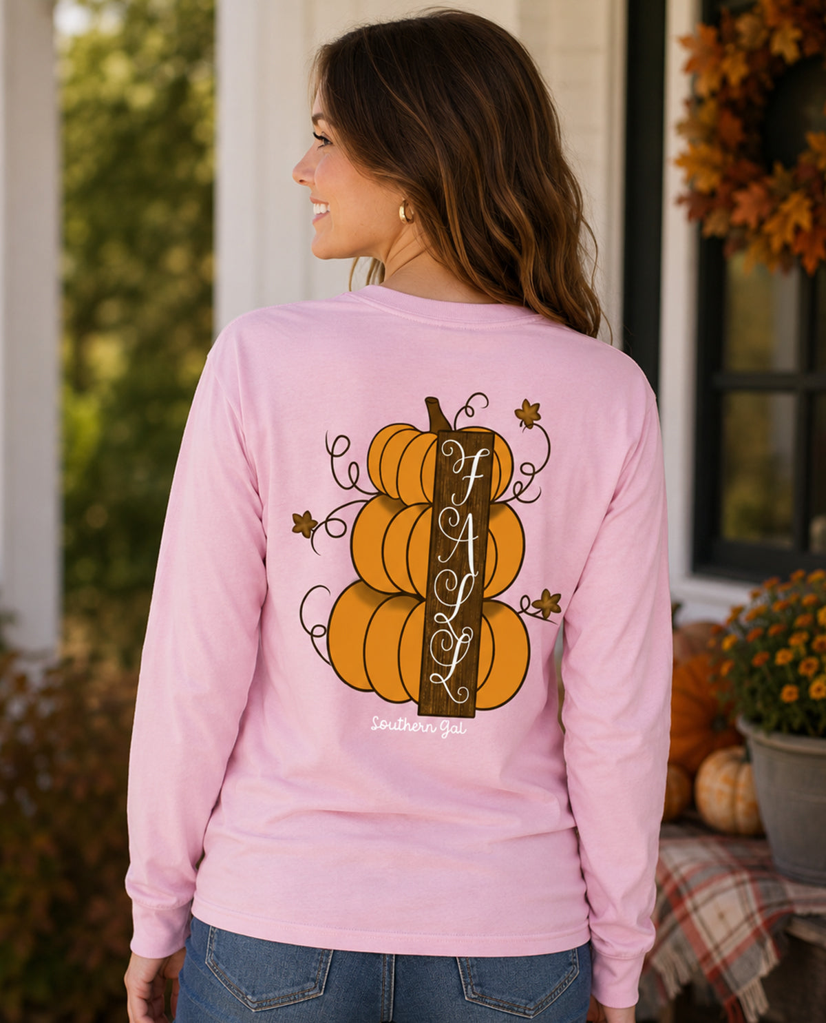 Woman wearing a pink long-sleeve shirt with pumpkins and 'FA L' text, standing outdoors.