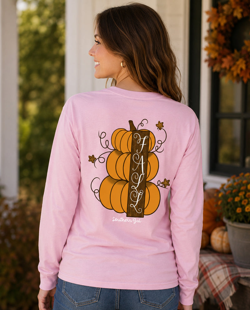 Woman wearing a pink long-sleeve shirt with pumpkins and 'FA L' text, standing outdoors.