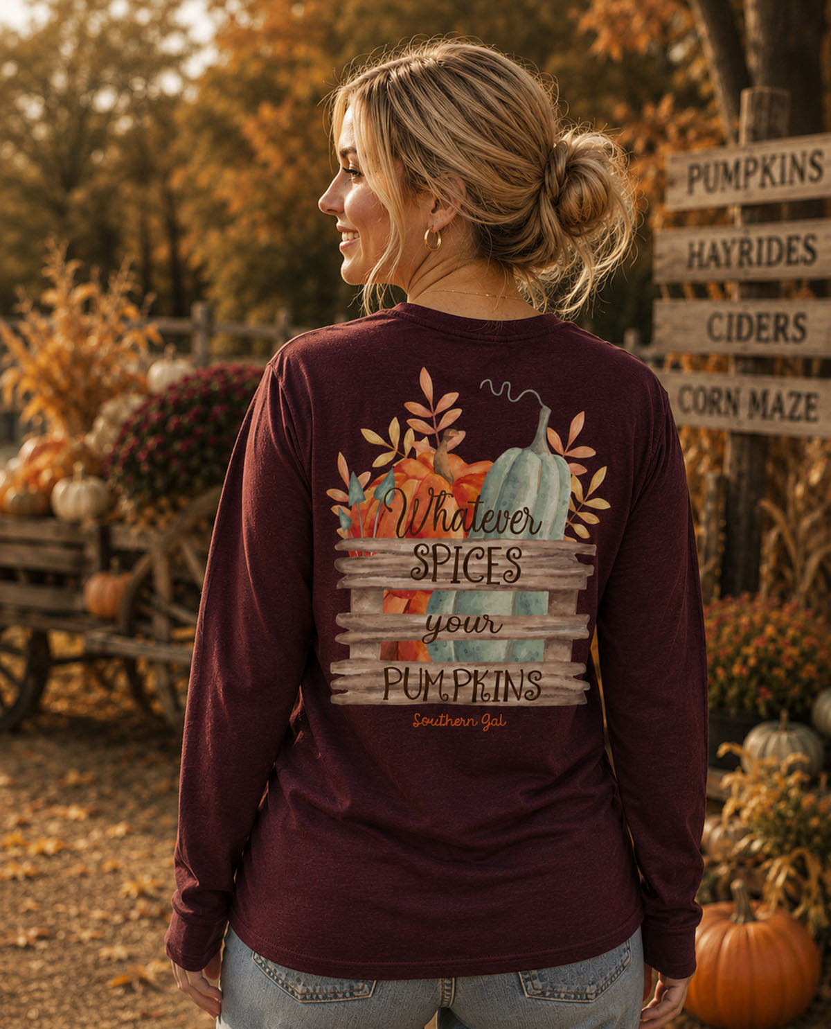 Woman wearing a maroon long-sleeve shirt with a fall-themed design in an autumn setting.