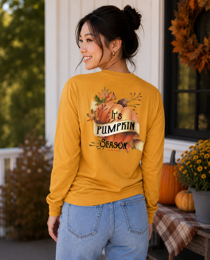 Woman wearing a mustard yellow long-sleeve shirt with 'It's Pumpkin Season' graphic on a porch.