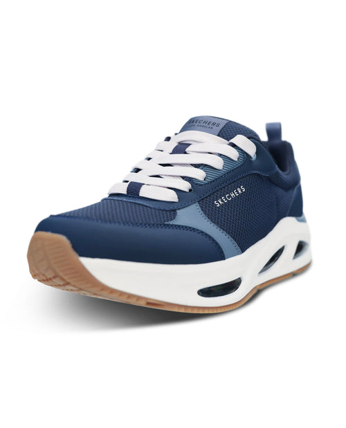 A Skechers sneaker in navy blue and white, featuring a chunky white midsole with a tan outsole, white laces, and the Skechers logo on the side.