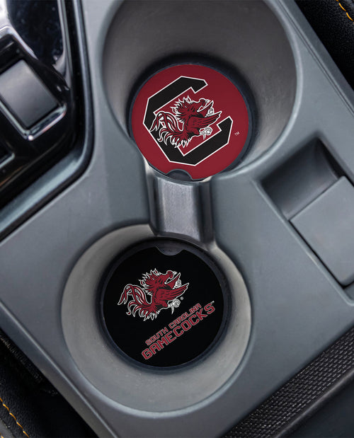 Two round car center console cup holder covers with South Carolina Gamecocks branding, one in red and black and one in black, installed in a gray console.