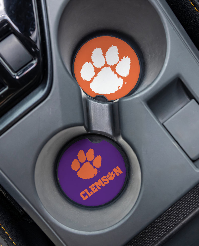 Two Clemson Tigers themed car cup holder coasters shown installed in a gray center console. The top coaster is orange with a white paw print, and the bottom coaster is purple with an orange paw print and the word 'CLEMSON'.