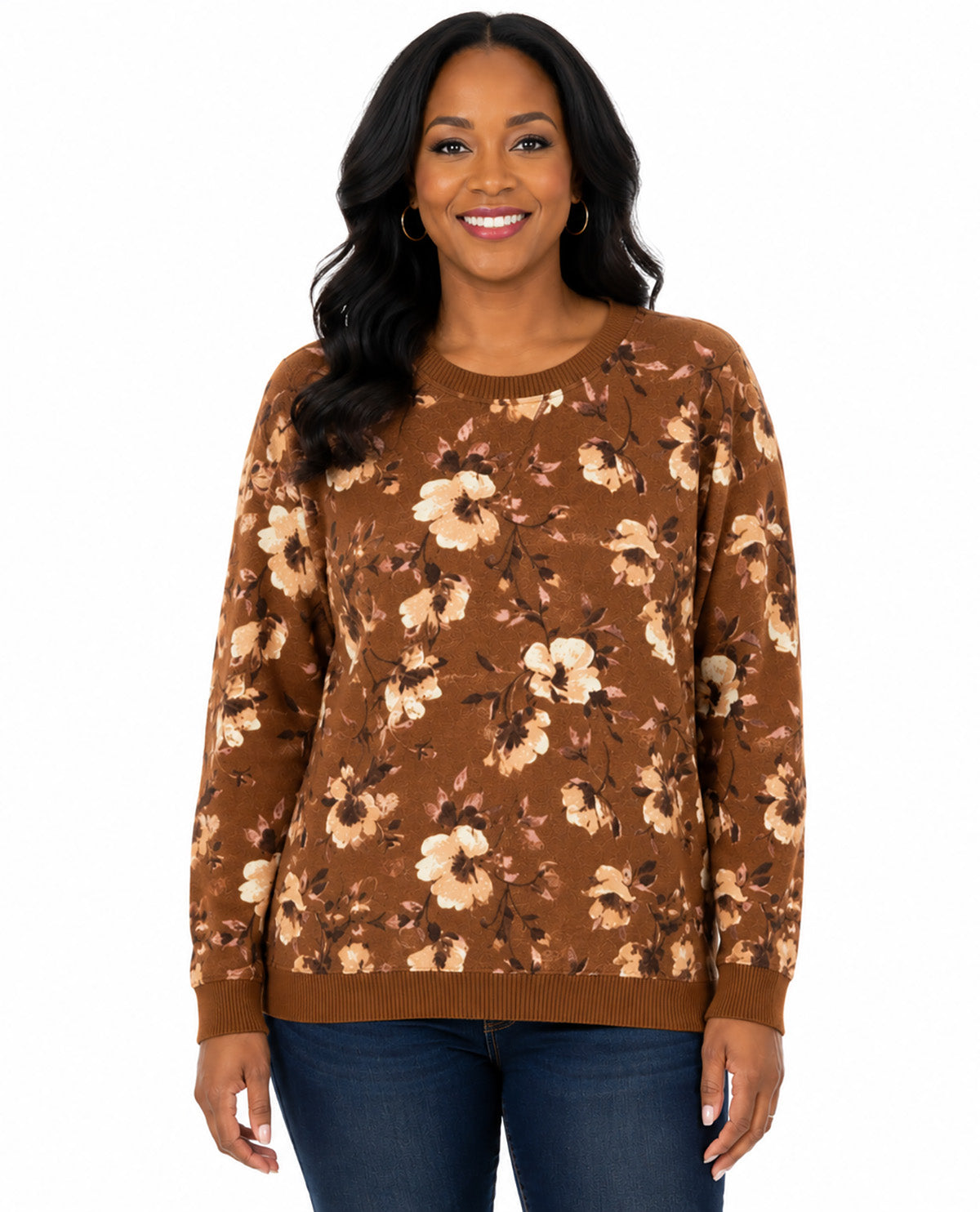 A woman wearing a brown crewneck sweater with a beige and brown floral pattern, paired with dark blue jeans, against a plain white background.