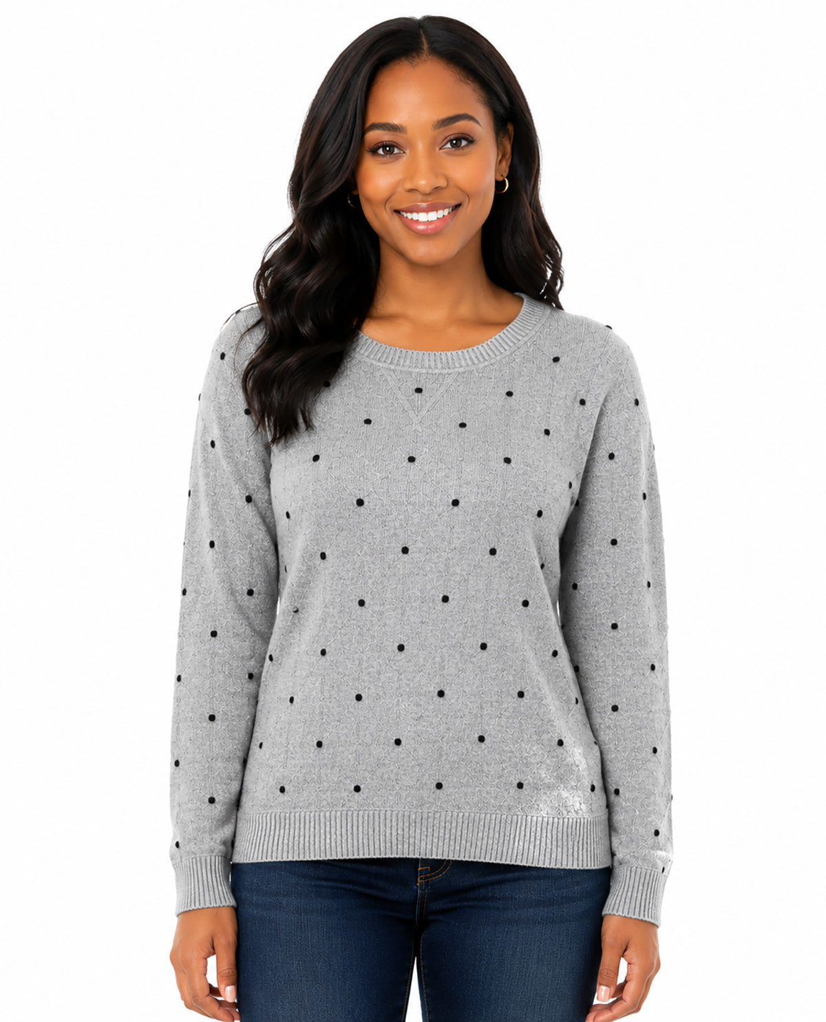 A woman modeling a light gray crewneck sweater with a black polka dot pattern, paired with dark blue jeans, against a plain white background.