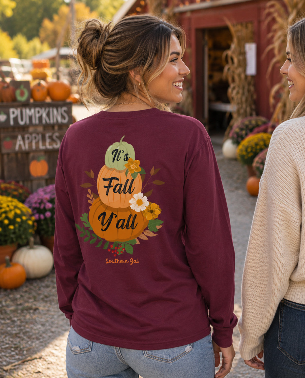 Woman wearing a maroon long-sleeve shirt with a fall-themed design at a pumpkin patch.