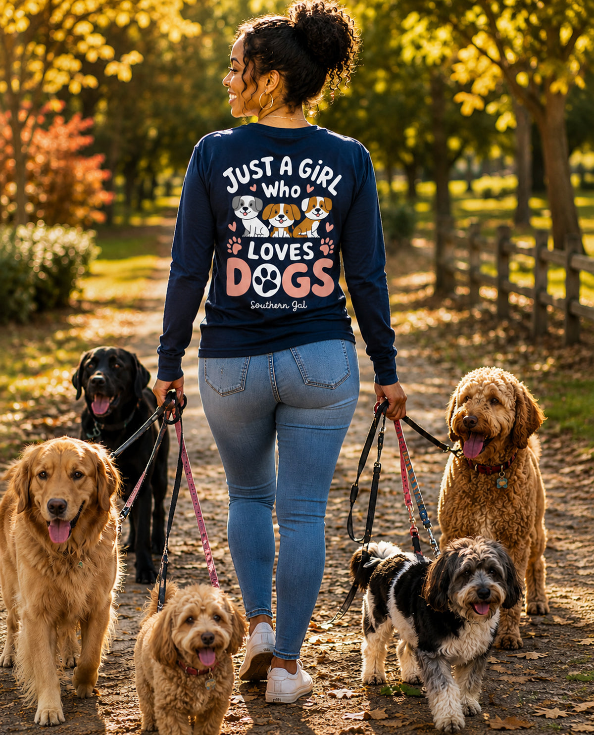 Woman walking multiple dogs in a park wearing a shirt that says 'Just a girl who loves dogs'.