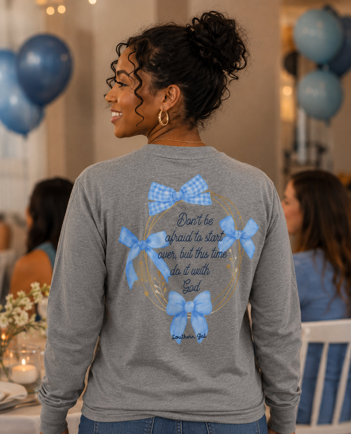 Woman wearing a gray long-sleeve shirt with blue bow design and text at an event with balloons.