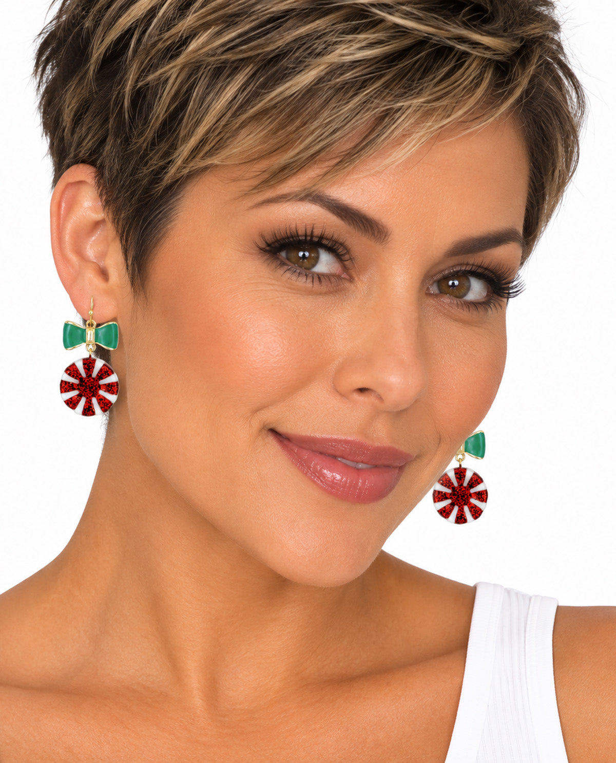 A close-up of a woman with short blonde-highlighted hair wearing festive dangle earrings. The earrings feature a green bow at the top with red and white candy cane snowflake charms hanging below, shown against a plain white background.