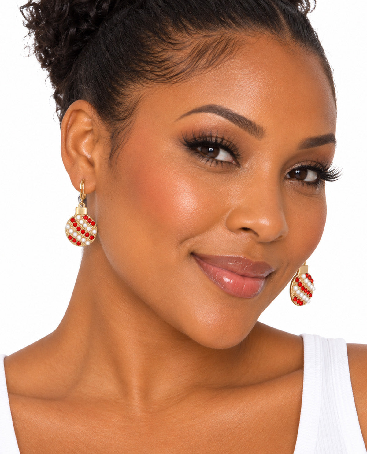 A close-up of a woman wearing gold dangle earrings with red and white striped candy cane patterns, set against a plain white background.
