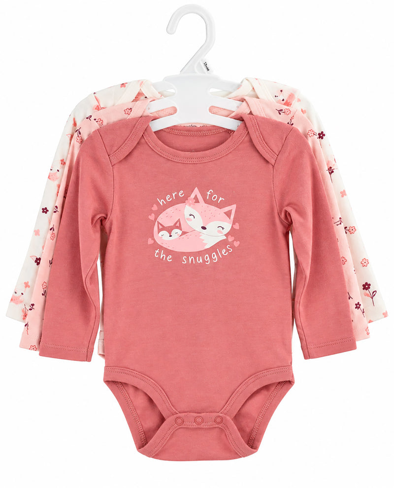 A set of three baby long-sleeve bodysuits on white hangers. The front bodysuit is dusty pink with a graphic of a sleeping fox and the text 'here for the snuggles'.