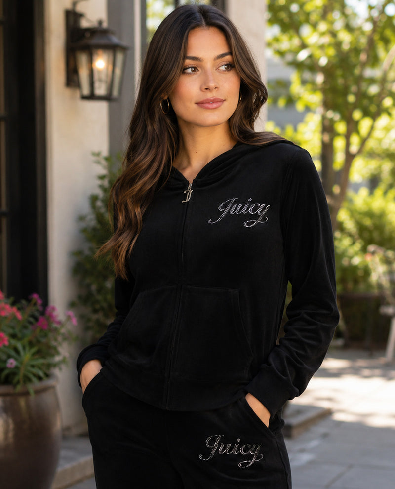 A woman wearing a black velvet zip-up hoodie with 'Juicy' embroidered in silver script on the chest, paired with matching black pants, set against an outdoor patio background.