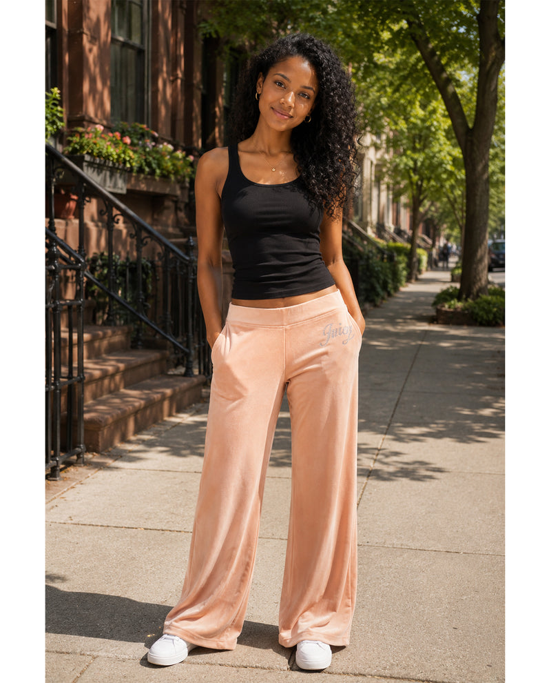 Woman wearing a black tank top and pink pants standing on a sidewalk with trees and buildings in the background.