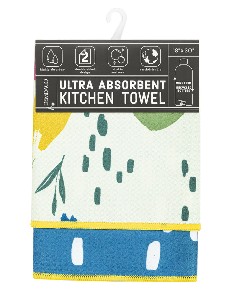 A packaged kitchen towel by Demaco, featuring a white towel with green leaf and droplet patterns and a blue bottom section, hanging against a plain white background.