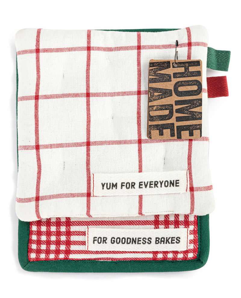 A square kitchen towel or potholder with a red and white grid pattern, green trim, and a hanging brown paper tag that reads 'HOME MADE'. A white fabric label on the front reads 'YUM FOR EVERYONE' and another label at the bottom reads 'FOR GOODNESS BAKES'.
