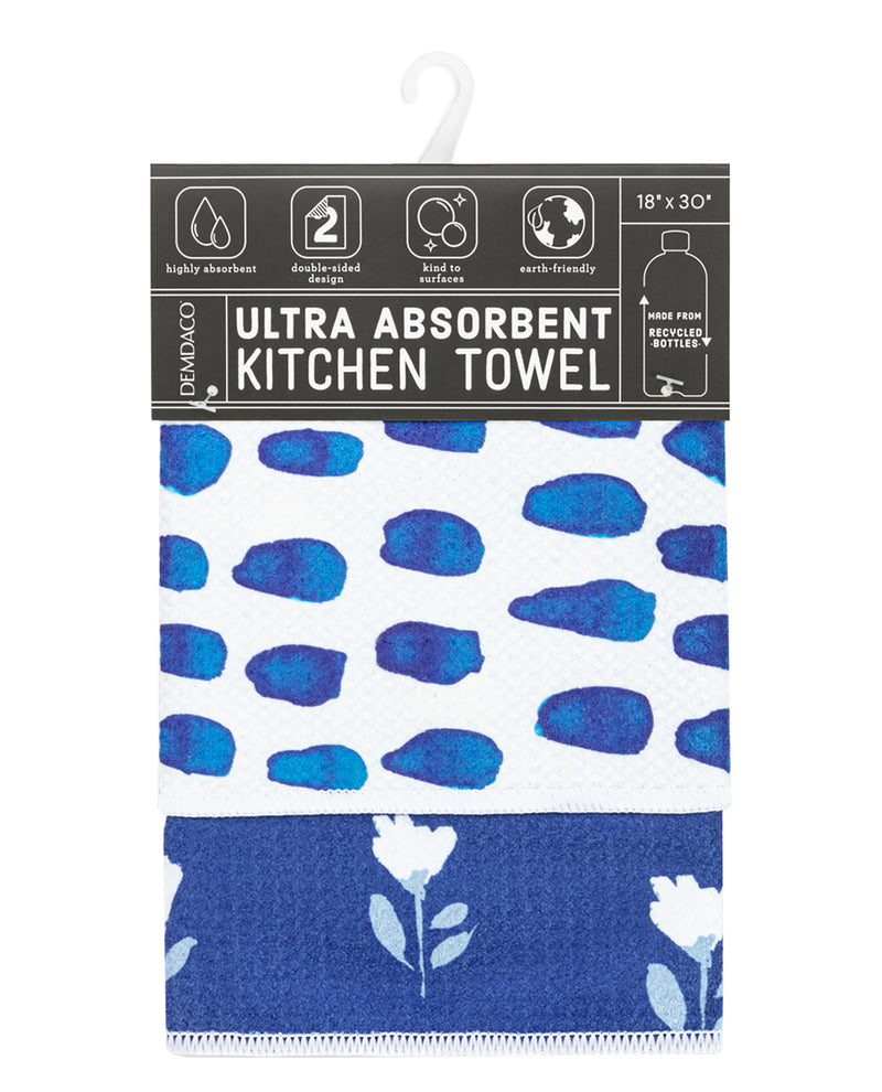 A packaged kitchen towel with a white upper section featuring blue abstract spots and a dark blue lower section with white floral motifs. The header card is dark gray/black with product features and dimensions.