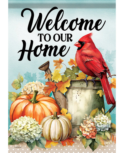 A decorative autumn-themed sign or print with the phrase “Welcome to our home” in large black script. The design shows a bright red cardinal perched on a metal bucket, with pumpkins, hydrangea flowers, and fall leaves around it on a light blue background.
