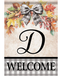 A fall-themed decorative sign or door mat with a large black script letter D in the center, a gray-and-white buffalo plaid bow at the top, autumn leaves and berries around it, and the word WELCOME in black text on a gray plaid band at the bottom.