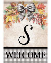 A decorative autumn-themed welcome sign with a faux-fur bow, colorful fall leaves, berries, and acorns at the top, a large black script letter S in the center, and the word WELCOME in black letters on a gray-and-white gingham band at the bottom.