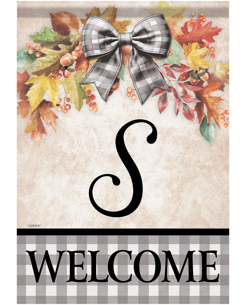 A decorative autumn-themed welcome sign with a faux-fur bow, colorful fall leaves, berries, and acorns at the top, a large black script letter S in the center, and the word WELCOME in black letters on a gray-and-white gingham band at the bottom.