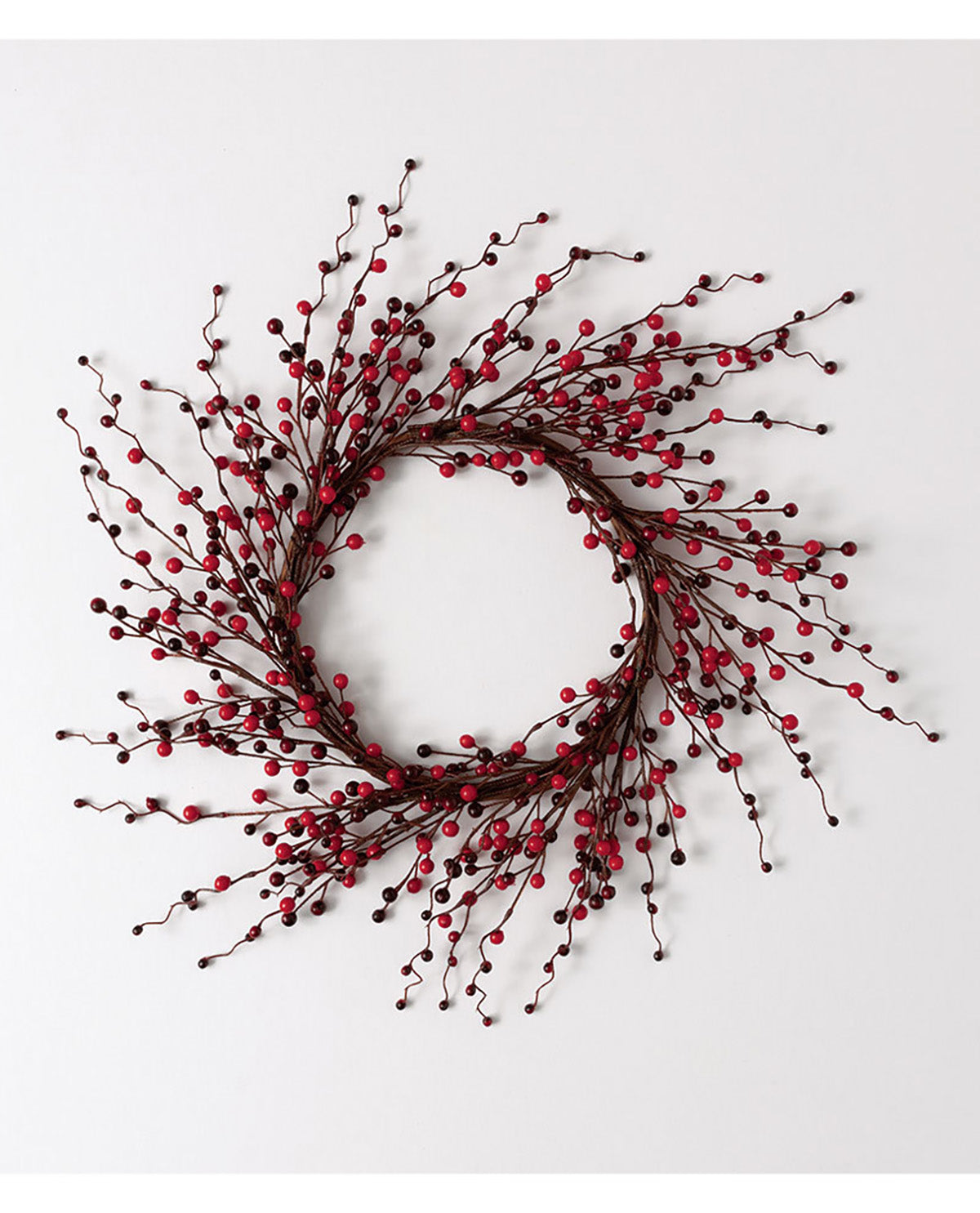 A decorative artificial wreath made of dark brown branches with clusters of small red berries, photographed against a plain light gray background.