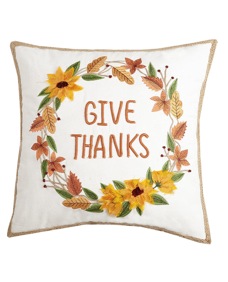 A square white throw pillow with a natural jute trim, featuring an embroidered autumn wreath with yellow sunflowers, orange and brown leaves, and the words 'GIVE THANKS' in orange-brown lettering in the center.