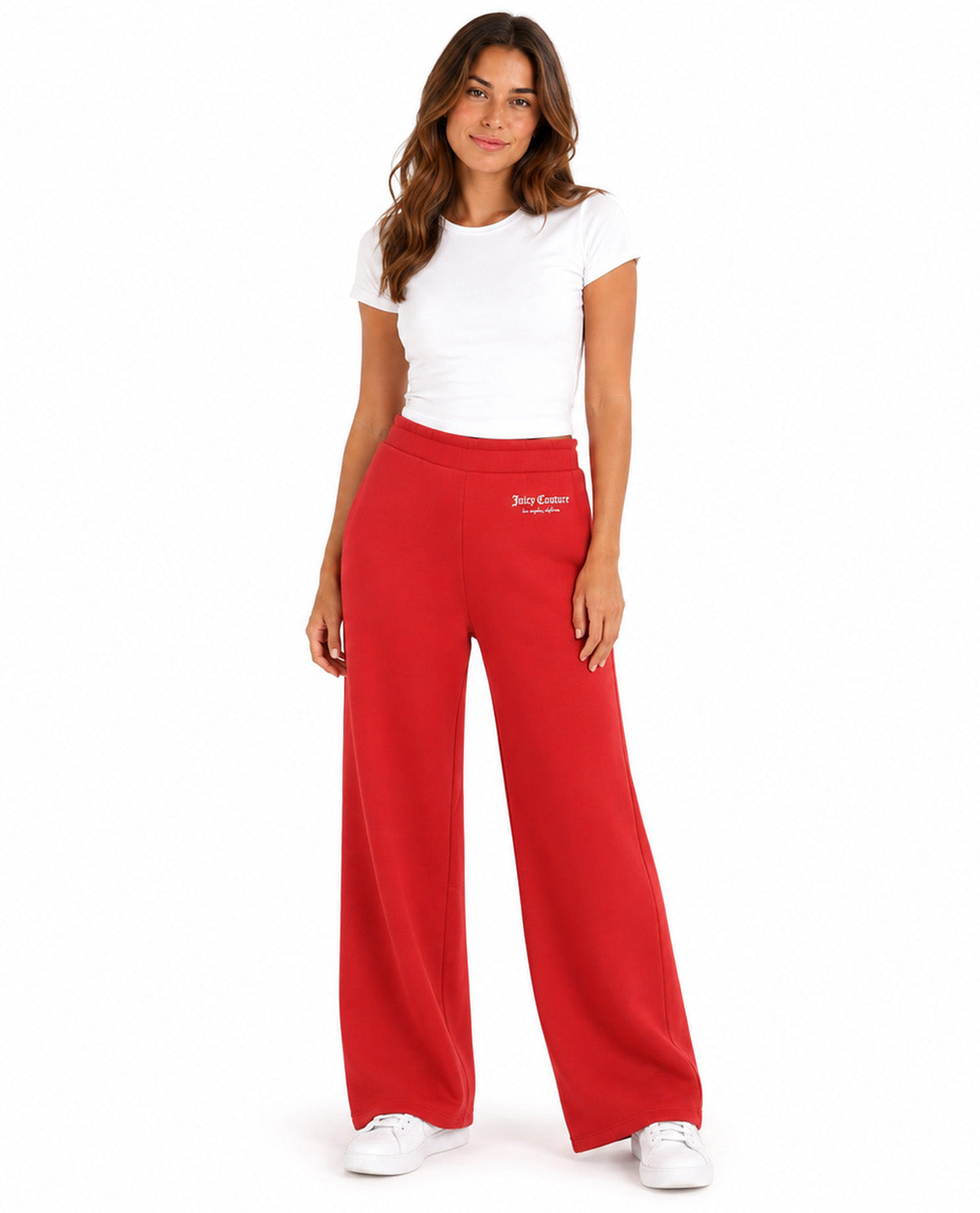 A woman modeling a pair of bright red wide-leg sweatpants with a small white embroidered logo on the left hip, paired with a white t-shirt and white sneakers, against a plain white background.