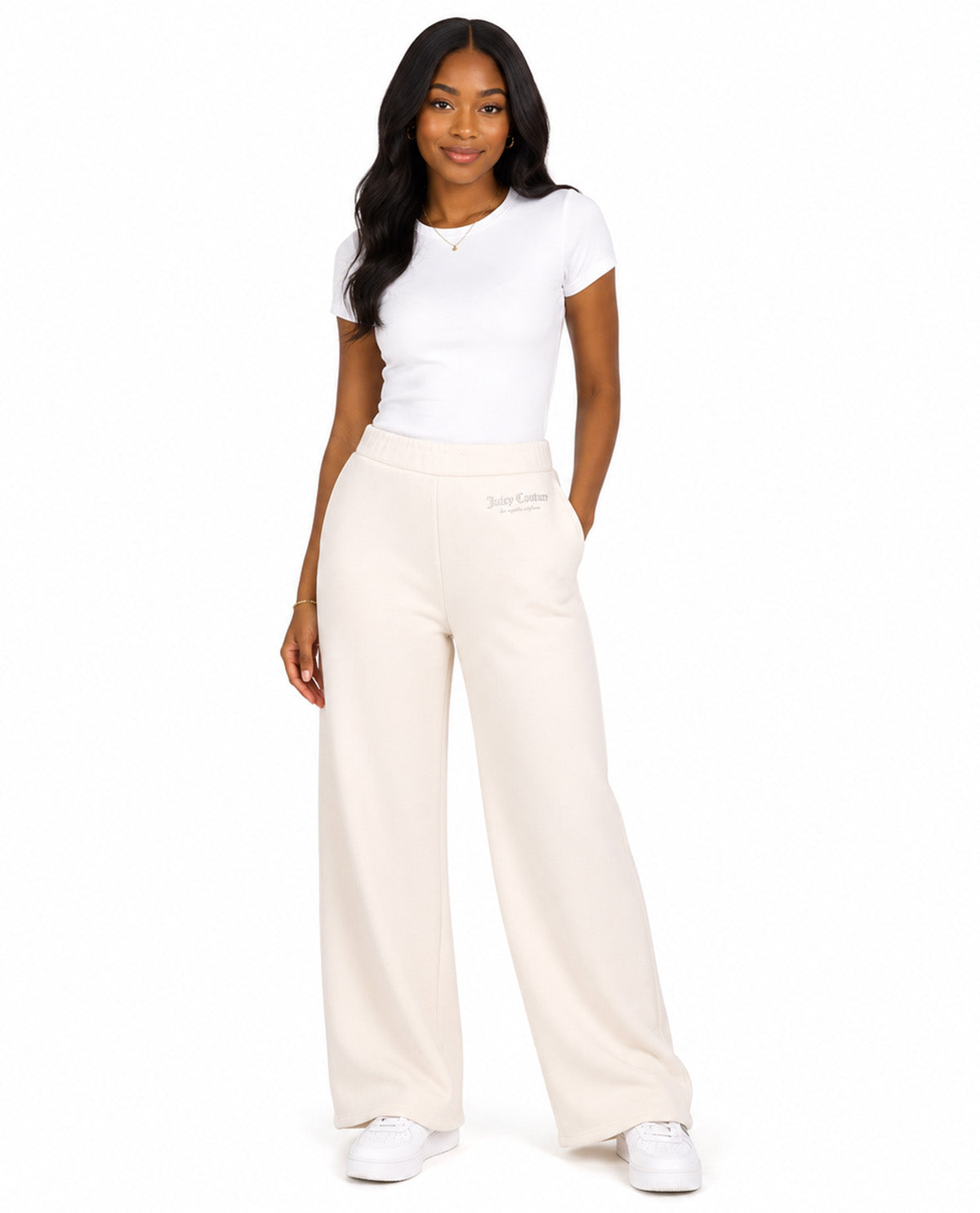 A woman modeling a pair of off-white wide-leg sweatpants with a white t-shirt and white sneakers, standing against a solid white background.